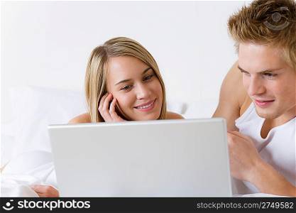 Young couple relax in bed with laptop lying down together