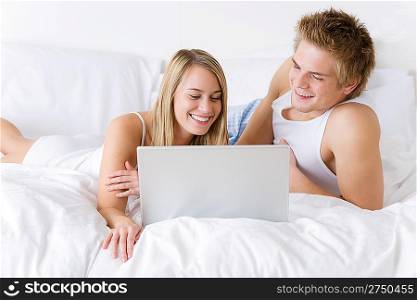 Young couple relax in bed with laptop lying down together