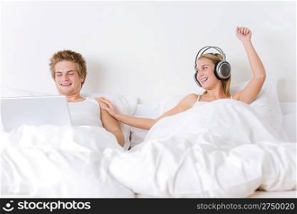 Young couple relax in bed with music and laptop together