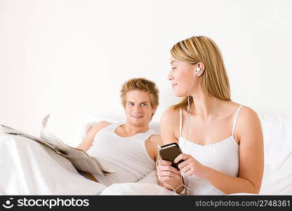 Young couple relax in white bed listen to music, read newspaper