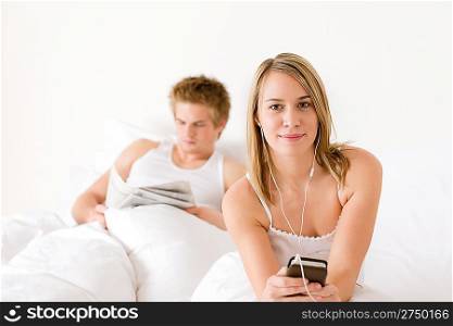 Young couple relax in white bed listen to music, read newspaper