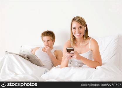 Young couple relax in white bed listen to music, read newspaper