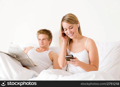 Young couple relax in white bed listen to music, read newspaper