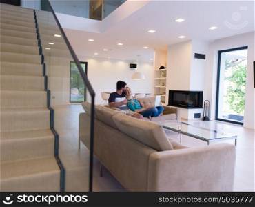 Young couple relaxes on the sofa in the luxury living room, using a laptop and remote control