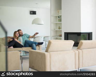 Young couple relaxes on the sofa in the luxury living room, using a tablet and remote control