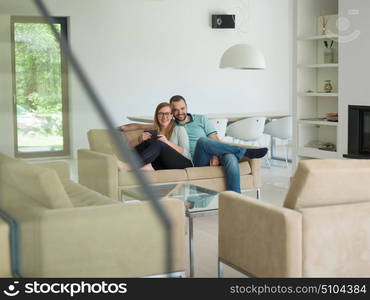 Young couple relaxes on the sofa in the luxury living room, using a tablet and remote control