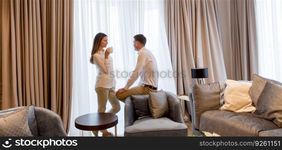 Young couple relaxing and talking with coffee cups in the luxurious room of contemporary apartment