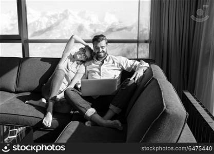 Young couple relaxing at home using laptop computers reading in the living room near the window on the sofa couch.. couple relaxing at home using laptop computers