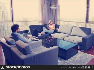 Young couple relaxing at home using tablet and laptop computers reading near the window on the sofa couch.. couple relaxing at home using tablet and laptop computers