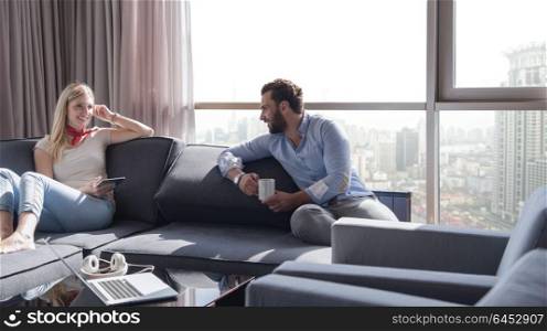 Young couple relaxing at home using tablet computer reading in the living room near the window on the sofa couch.