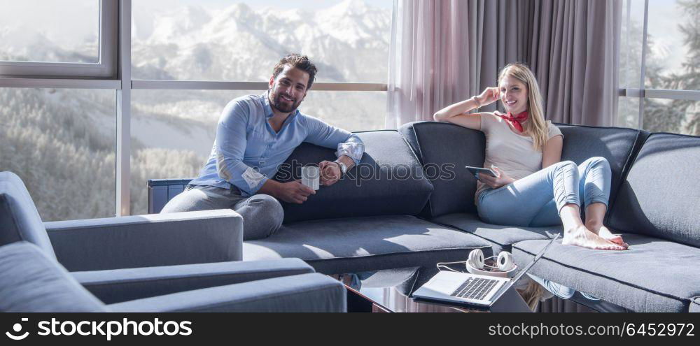 Young couple relaxing at home using tablet computer reading in the living room near the window on the sofa couch.