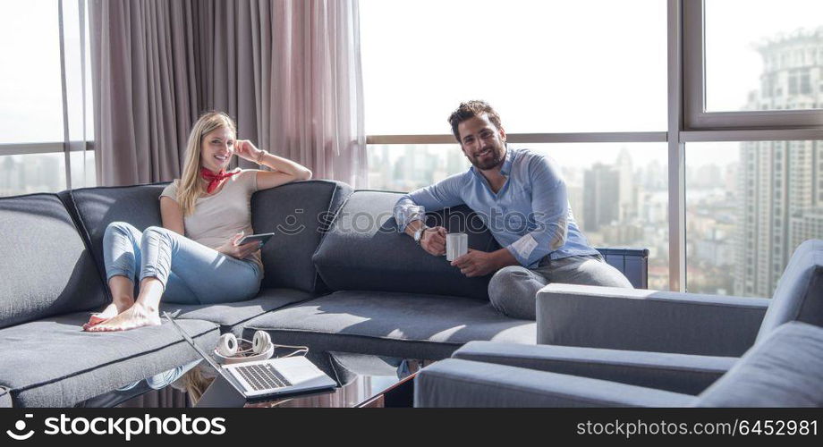 Young couple relaxing at home using tablet computer reading in the living room near the window on the sofa couch.