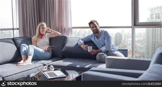 Young couple relaxing at home using tablet computer reading in the living room near the window on the sofa couch.