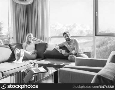 Young couple relaxing at home using tablet computer reading in the living room near the window on the sofa couch.. couple relaxing at home using tablet computer
