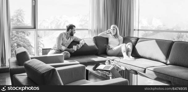 Young couple relaxing at home using tablet computer reading in the living room near the window on the sofa couch.. couple relaxing at home using tablet computer