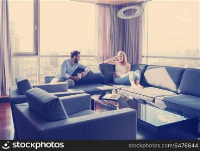 Young couple relaxing at home using tablet computer reading in the living room near the window on the sofa couch.. couple relaxing at home using tablet computer