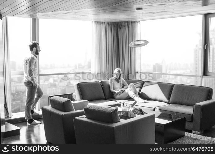 Young couple relaxing at home using tablet computer reading in the living room near the window on the sofa couch.. couple relaxing at home using tablet computer