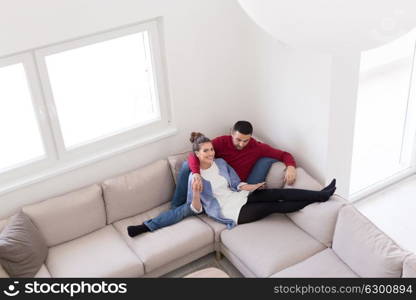 Young couple relaxing at home using tablet computers reading in the living room on the sofa couch.