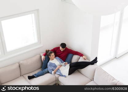 Young couple relaxing at home using tablet computers reading in the living room on the sofa couch.