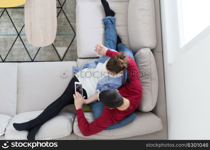 Young couple relaxing at home using tablet computers reading in the living room on the sofa couch.