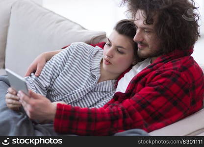 Young couple relaxing at home using tablet computers reading in the living room on the sofa couch.