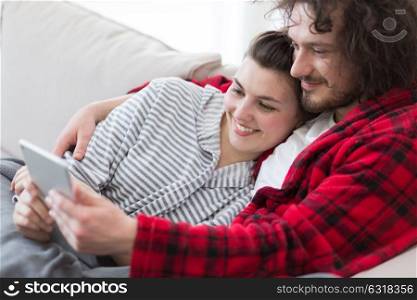 Young couple relaxing at home using tablet computers reading in the living room on the sofa couch.