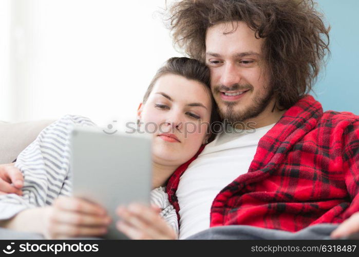 Young couple relaxing at home using tablet computers reading in the living room on the sofa couch.