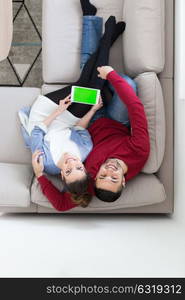 Young couple relaxing at home using tablet computers reading in the living room on the sofa couch.