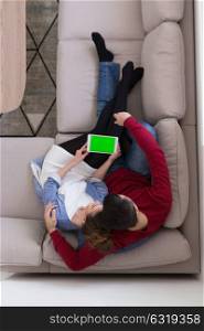 Young couple relaxing at home using tablet computers reading in the living room on the sofa couch.