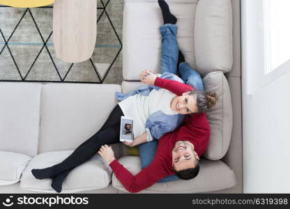 Young couple relaxing at home using tablet computers reading in the living room on the sofa couch.