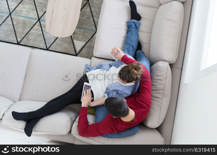 Young couple relaxing at home using tablet computers reading in the living room on the sofa couch.