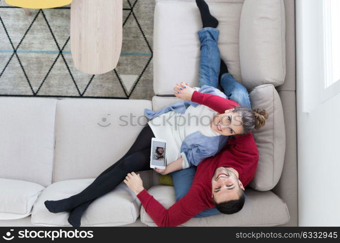 Young couple relaxing at home using tablet computers reading in the living room on the sofa couch.