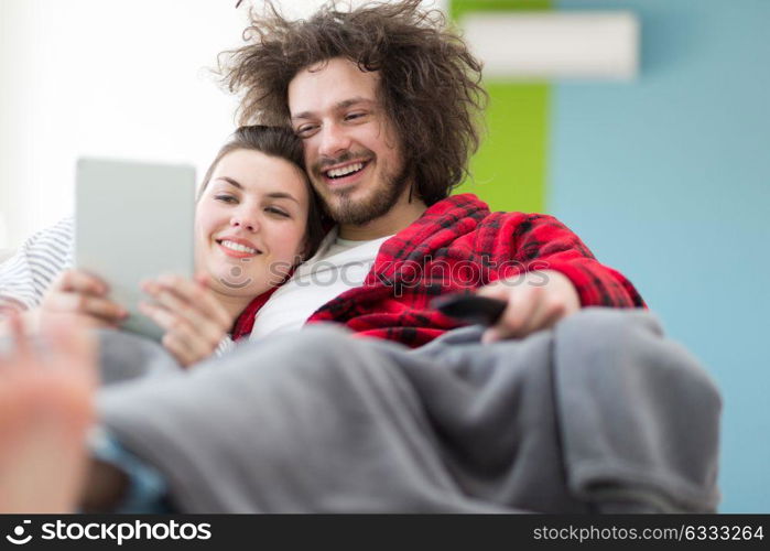 Young couple relaxing at home using tablet computers reading in the living room on the sofa couch.