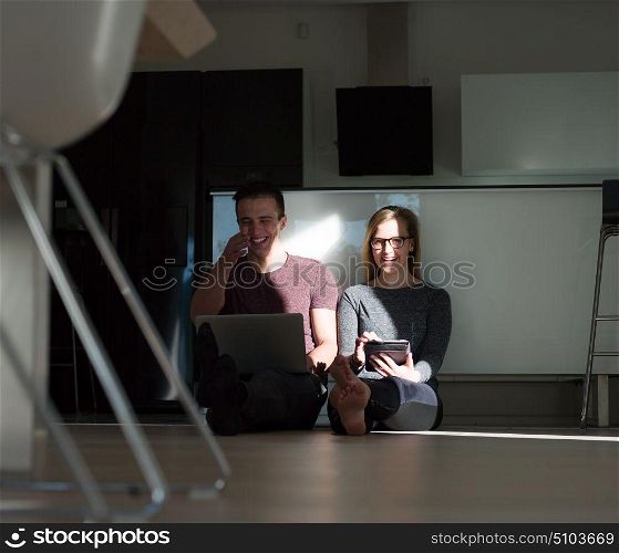 Young couple relaxing at luxurious home with tablet and laptop computers reading on the floor