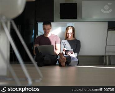 Young couple relaxing at luxurious home with tablet and laptop computers reading on the floor