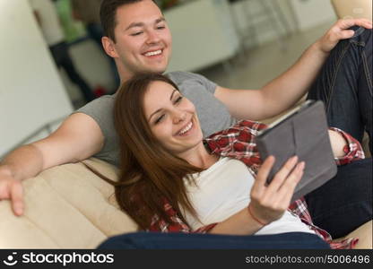 Young couple relaxing at luxurious home with tablet computers reading in the living room on the sofa couch.