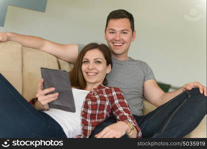 Young couple relaxing at luxurious home with tablet computers reading in the living room on the sofa couch.