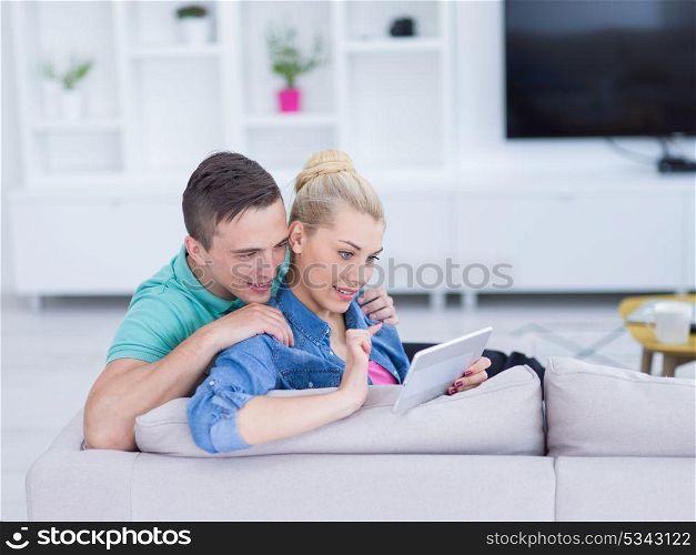 Young couple relaxing at luxurious home with tablet computers reading in the living room on the sofa couch.