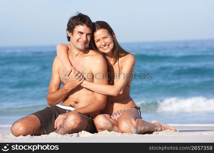 Young Couple Relaxing On Beach Wearing Swimwear