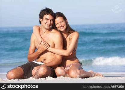 Young Couple Relaxing On Beach Wearing Swimwear