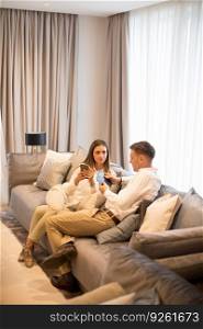 Young couple relaxing on couch in luxury living room and using mobile phone
