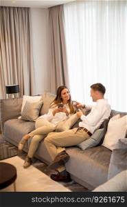Young couple relaxing on couch in luxury living room and using mobile phone