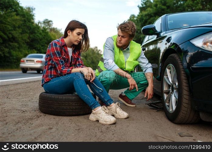 Young couple repair flat tyre, car breakdown. Broken automobile or emergency accident with vehicle, trouble with punctured auto tire on highway