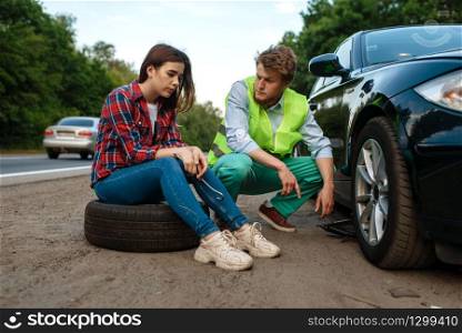 Young couple repair flat tyre, car breakdown. Broken automobile or emergency accident with vehicle, trouble with punctured auto tire on highway
