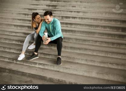 Young couple resting during training with bottle of water in urban environment