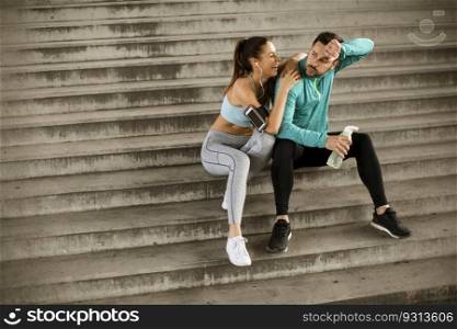Young couple resting during training with bottle of water in urban environment
