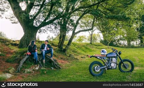 Young couple resting from a motorcycle trip having a beer outdoors. Couple resting from a motorcycle trip
