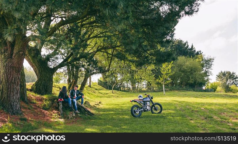 Young couple resting from a motorcycle trip having a beer outdoors. Couple resting from a motorcycle trip