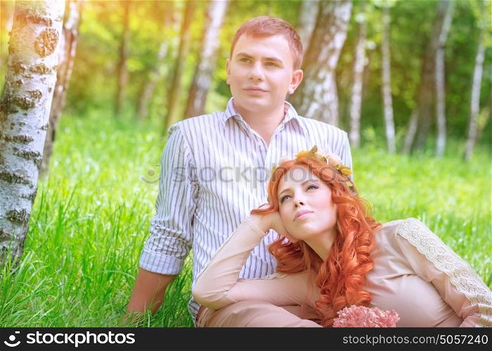Young couple resting in the park, handsome man sitting on the grass and his beautiful girlfriend lying down on his legs, love and romantic date concept
