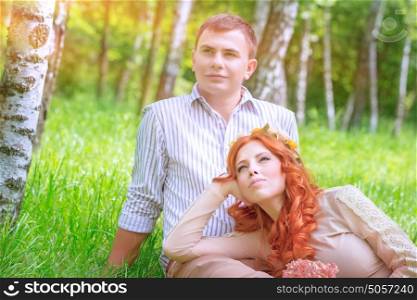 Young couple resting in the park, handsome man sitting on the grass and his beautiful girlfriend lying down on his legs, love and romantic date concept